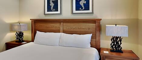 A hotel room with a wooden headboard, two framed seahorse artworks, a white bedspread, and two bedside tables with lamps.