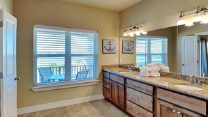 A bathroom with a large window, wooden cabinets, a sink, and a mirror with lights.