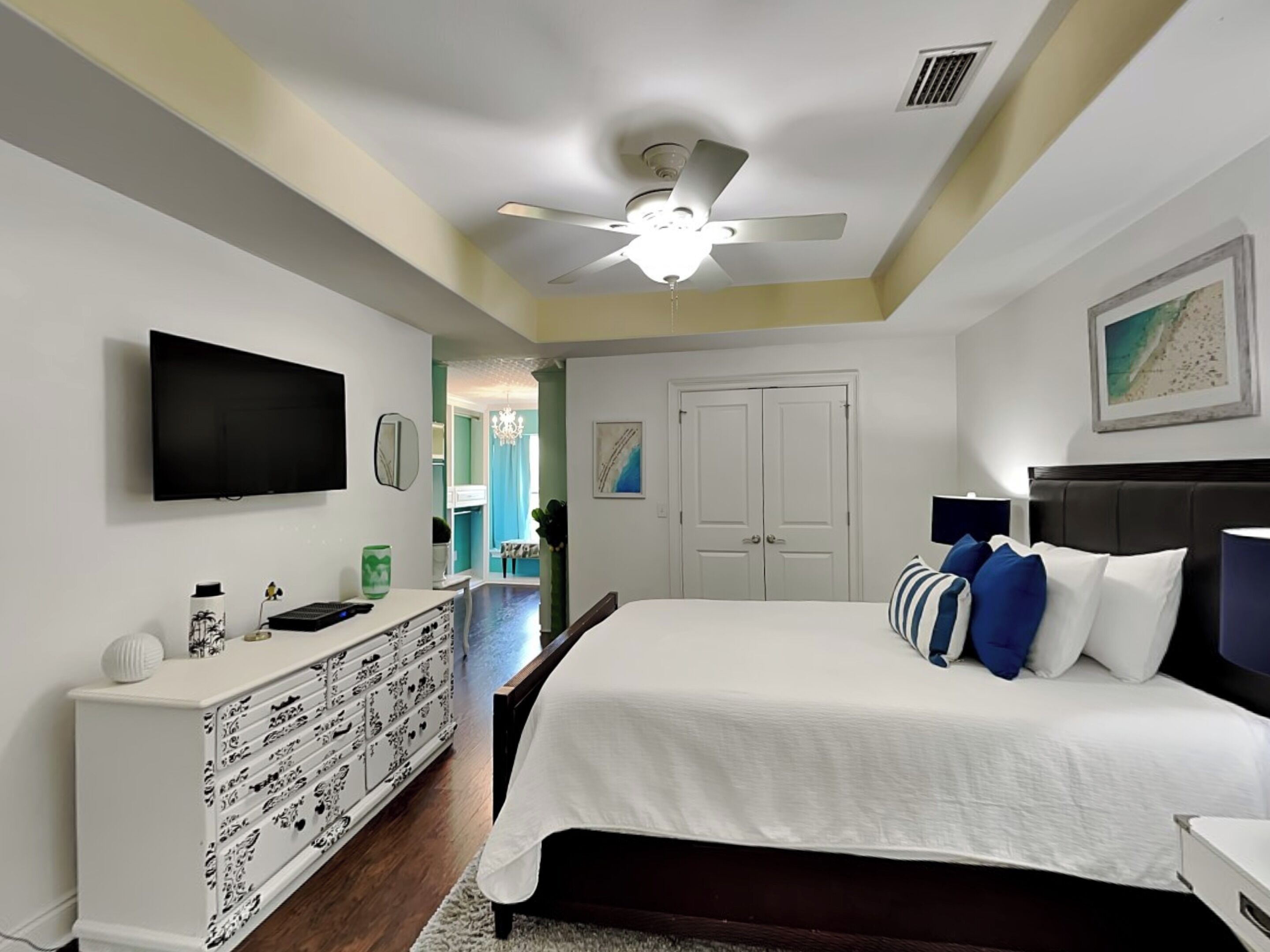 A bedroom with a bed, a dresser, a television, and a ceiling fan.