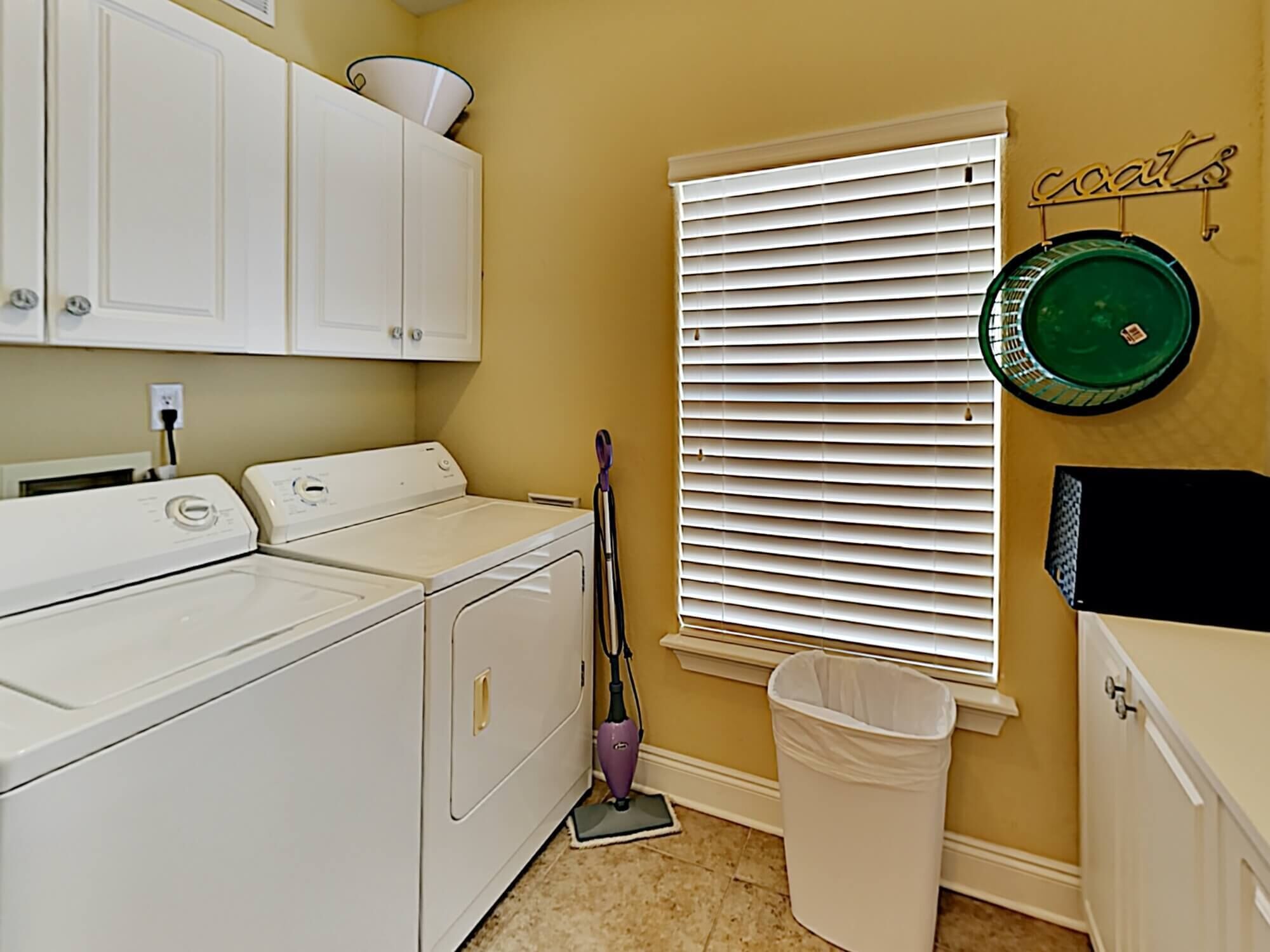 A laundry room with a washing machine, dryer, and a mop leaning against the wall.