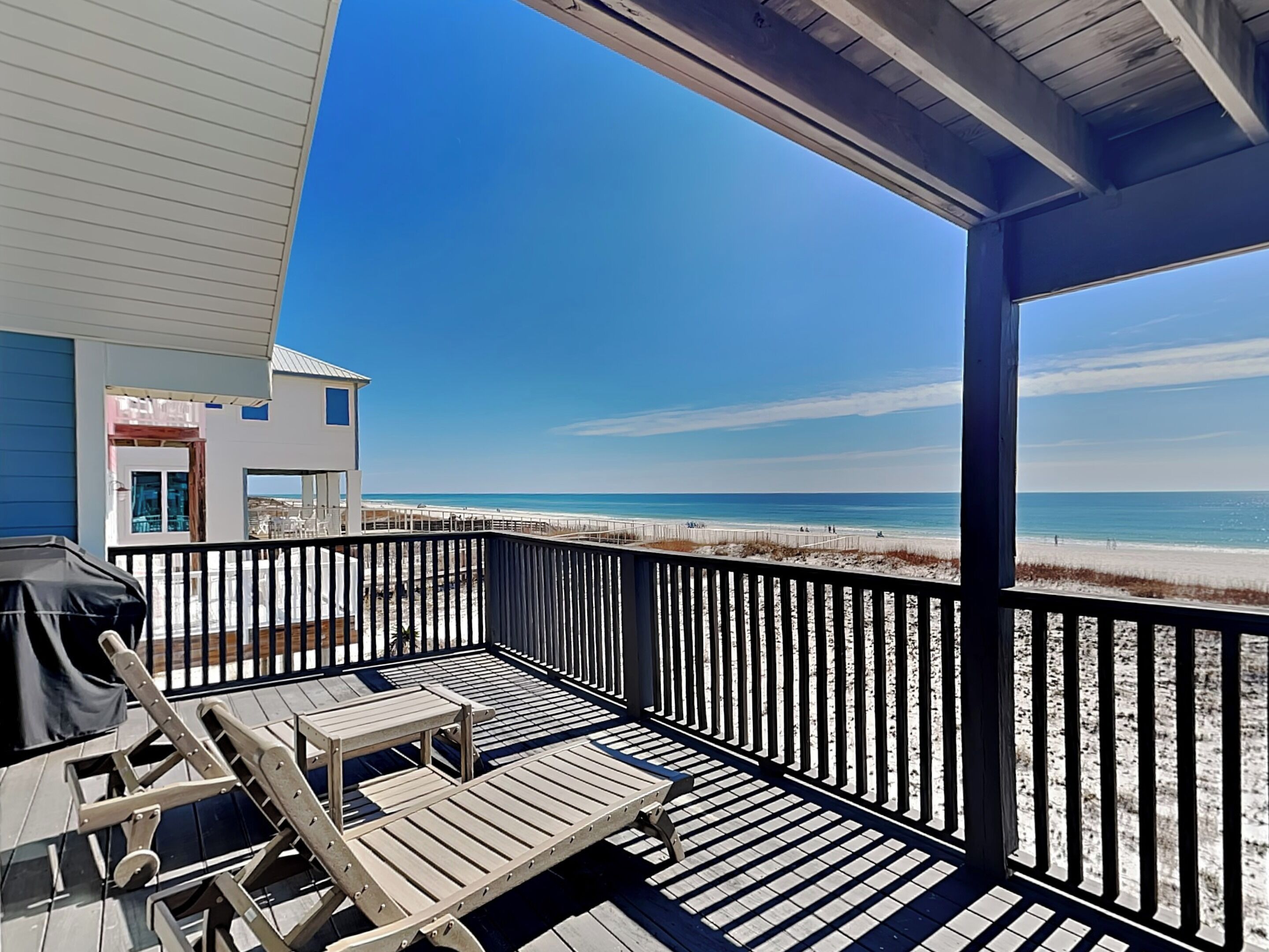 Une terrasse en bois avec un barbecue et un espace salon donnant sur une plage.