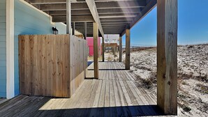 Eine Holzterrasse mit überdachtem Bereich, Holzsäulen und Blick auf den Strand.