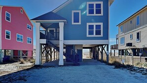Ein Strandhaus mit überdachter Veranda und einer Treppe zu einer zweiten Ebene.
