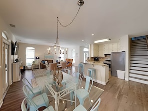 A spacious kitchen with a central island, a dining area with a glass table and chairs, and a staircase on the right.