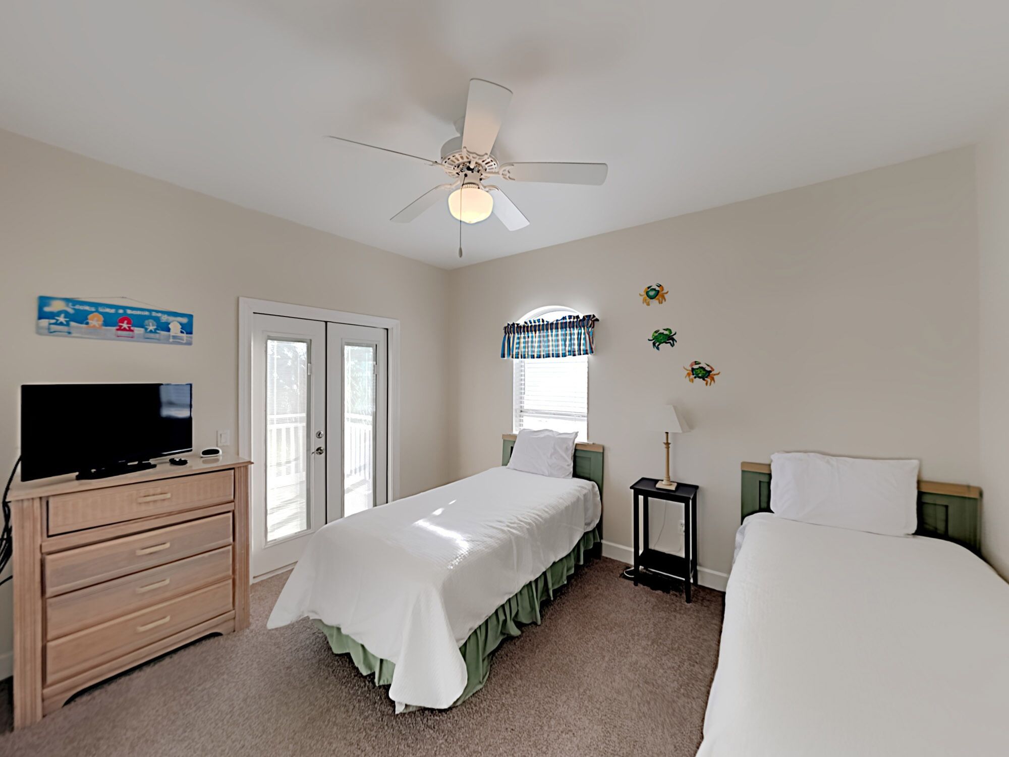 A bedroom with a bed, a dresser, a television, a ceiling fan, and a window with curtains.