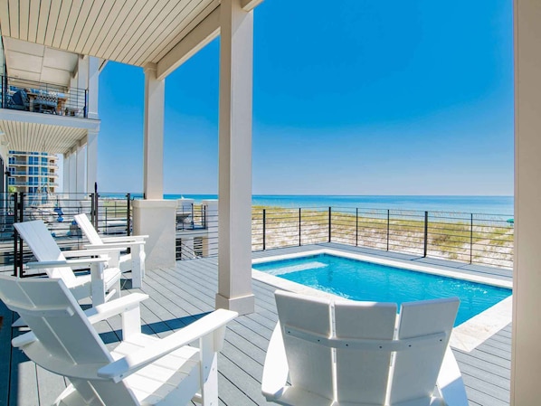 Zona junto a la piscina con sillas blancas y vista a la playa.