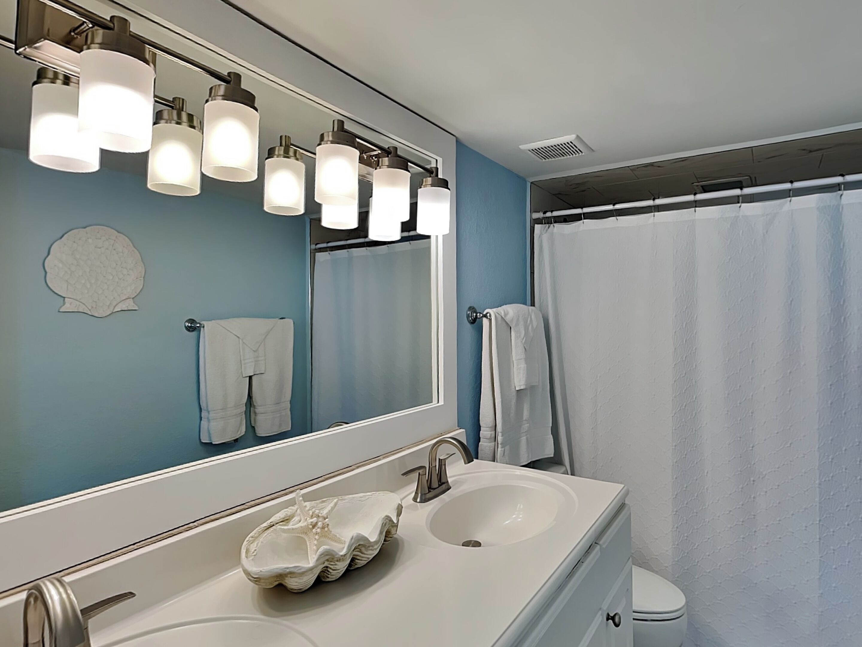 Une salle de bain avec un lavabo blanc, un grand miroir et un rideau de douche.