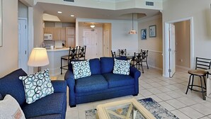 A spacious living room with a blue sofa set, a coffee table, and a dining area with chairs and a table. - Silver Beach Towers #1805E by Southern Vacation Rentals (Destin)