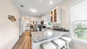 A modern kitchen with white cabinetry, granite countertops, a stainless steel refrigerator, and a window with a view of palm trees. - Salt & Sand - Serenity on 30A - Hidden Lakes Condo 321 (Santa Rosa Beach)