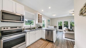 A modern kitchen with white cabinets, a built-in microwave, stainless steel appliances, and a large window providing natural light. - Salt & Sand - Serenity on 30A - Hidden Lakes Condo 321 (Santa Rosa Beach)