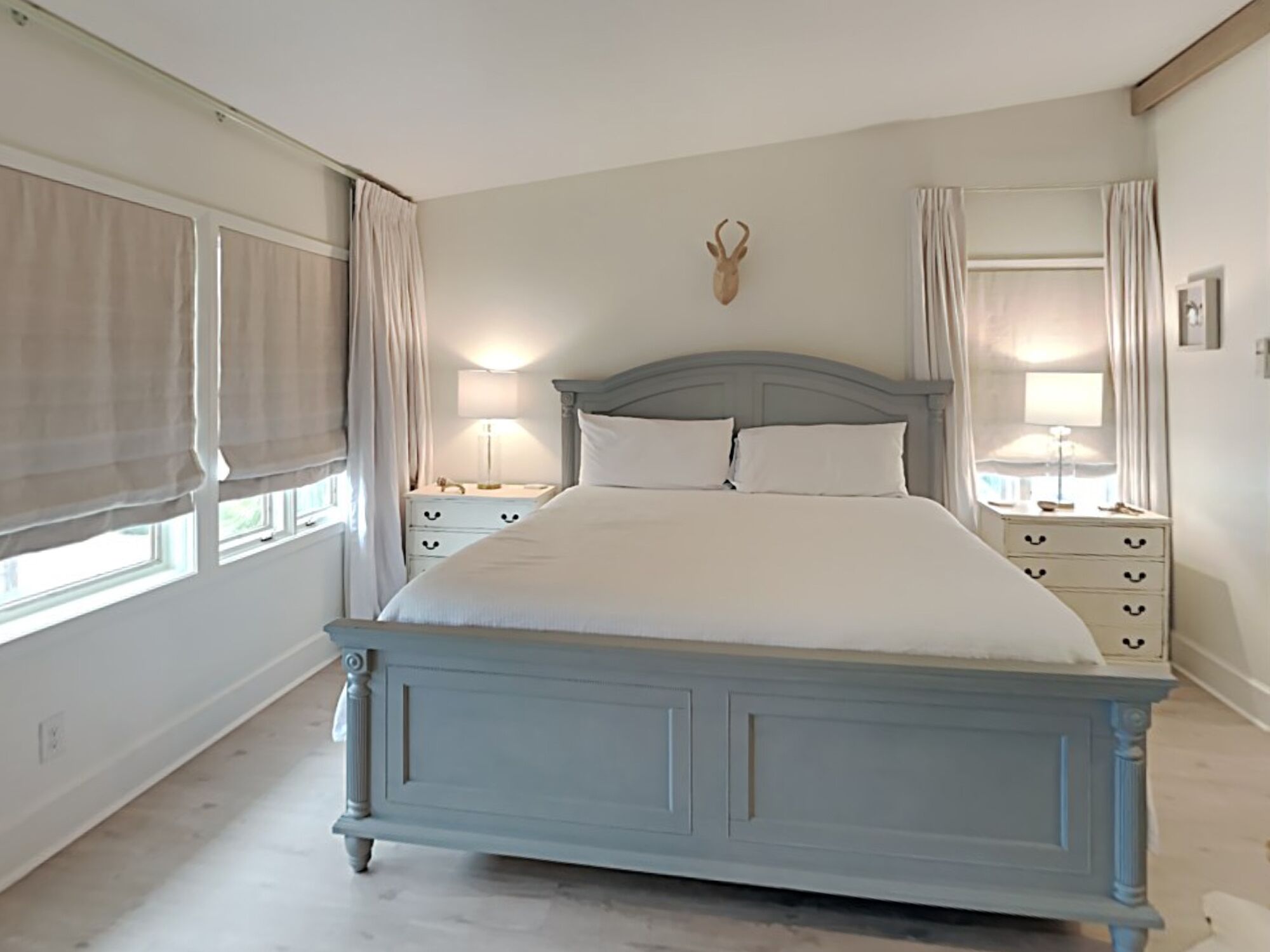 A bedroom with a bed, bedside tables, a wall-mounted deer head decoration, and a window with curtains.