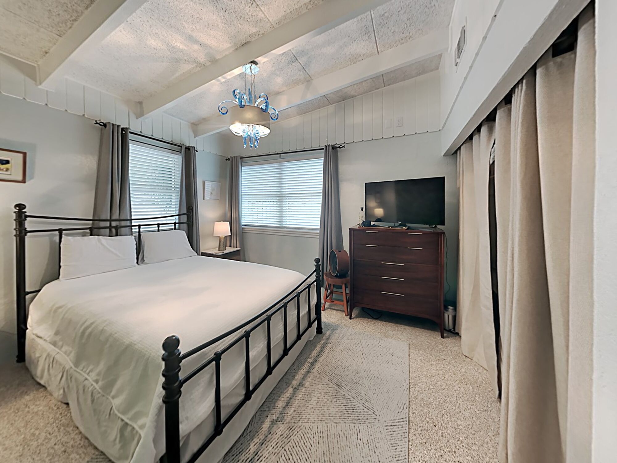 A bedroom with a bed, a dresser, a television, and a chandelier.