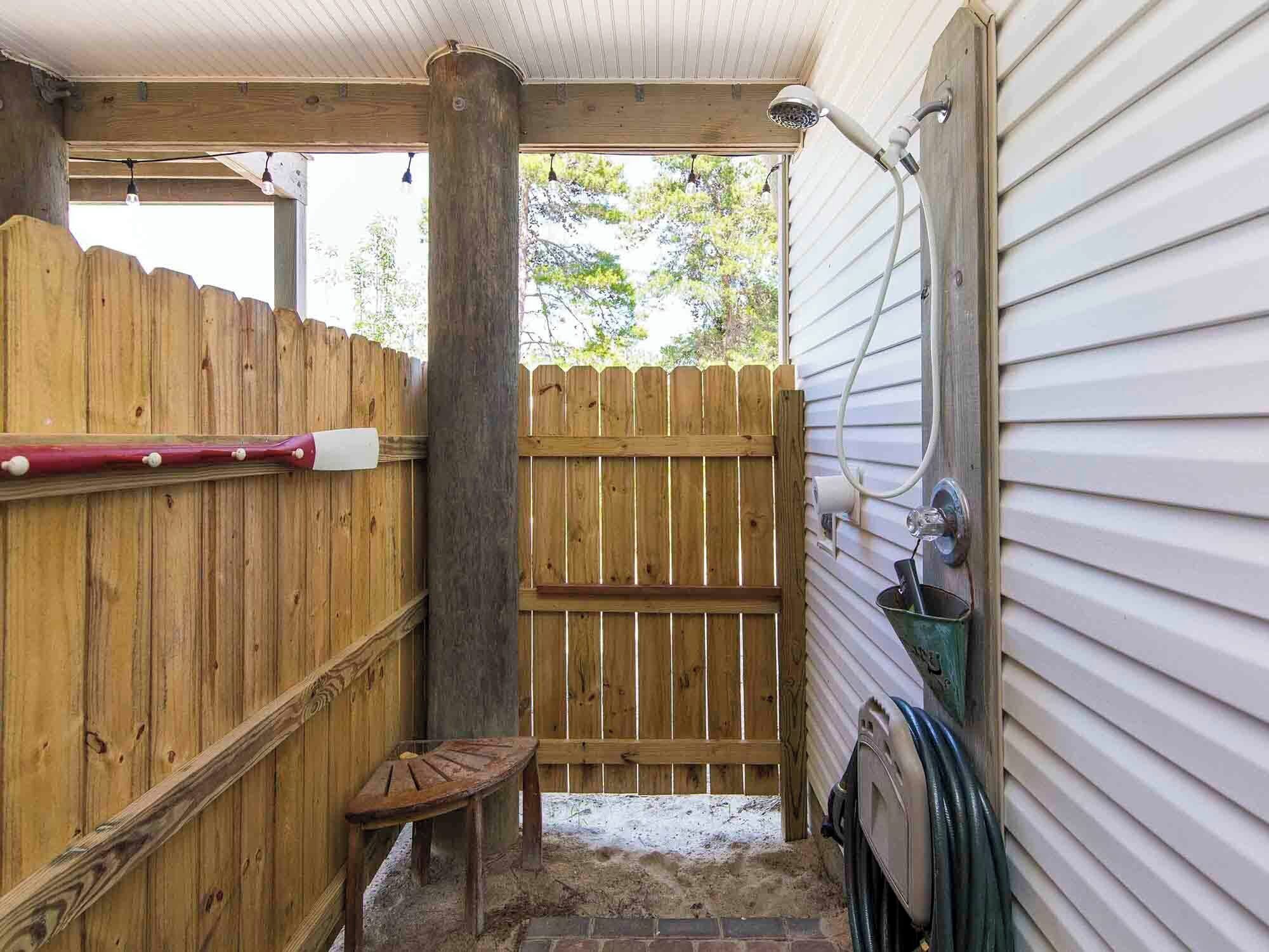 A covered outdoor area with a wooden bench, a wooden fence, and a hose connected to a metal faucet.