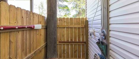 A covered outdoor area with a wooden bench, a wooden fence, and a hose connected to a metal faucet.