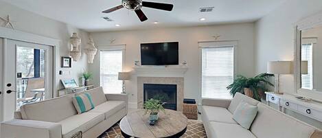 A living room with a ceiling fan, a fireplace, a television, and wicker furniture.
