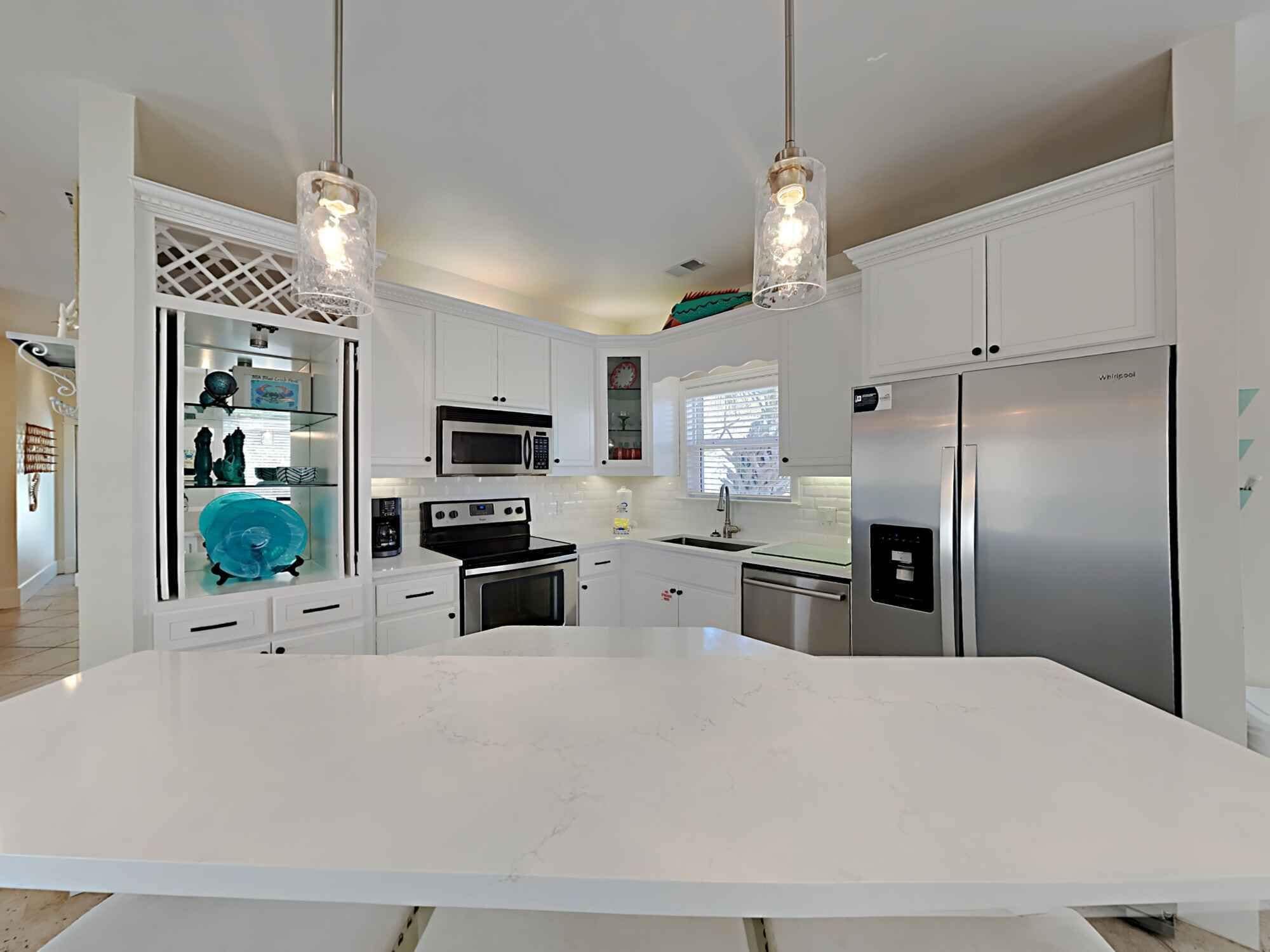 Una cocina moderna con armarios blancos, electrodomésticos de acero inoxidable, una isla grande e iluminación colgante.