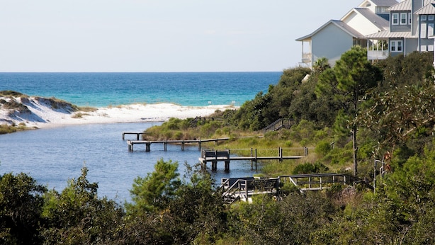 A coastal property with a wooden dock extending into a calm sea, surrounded by lush greenery and a white building with a balcony. - Aloha Sandy Bay by Southern Vacation Rentals (Santa Rosa Beach)