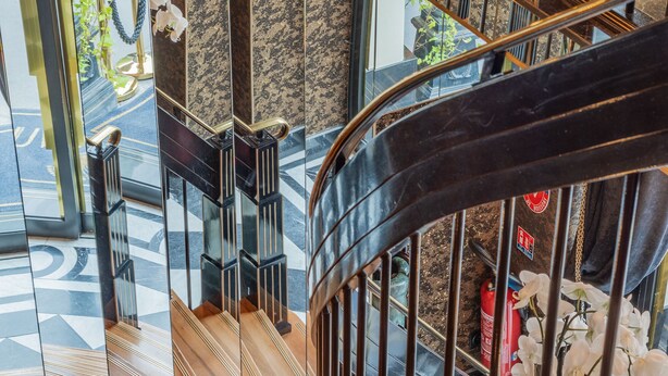 A modern interior with a spiral staircase, reflective surfaces, and a view of the street below. - Manolita Paris (Paris)