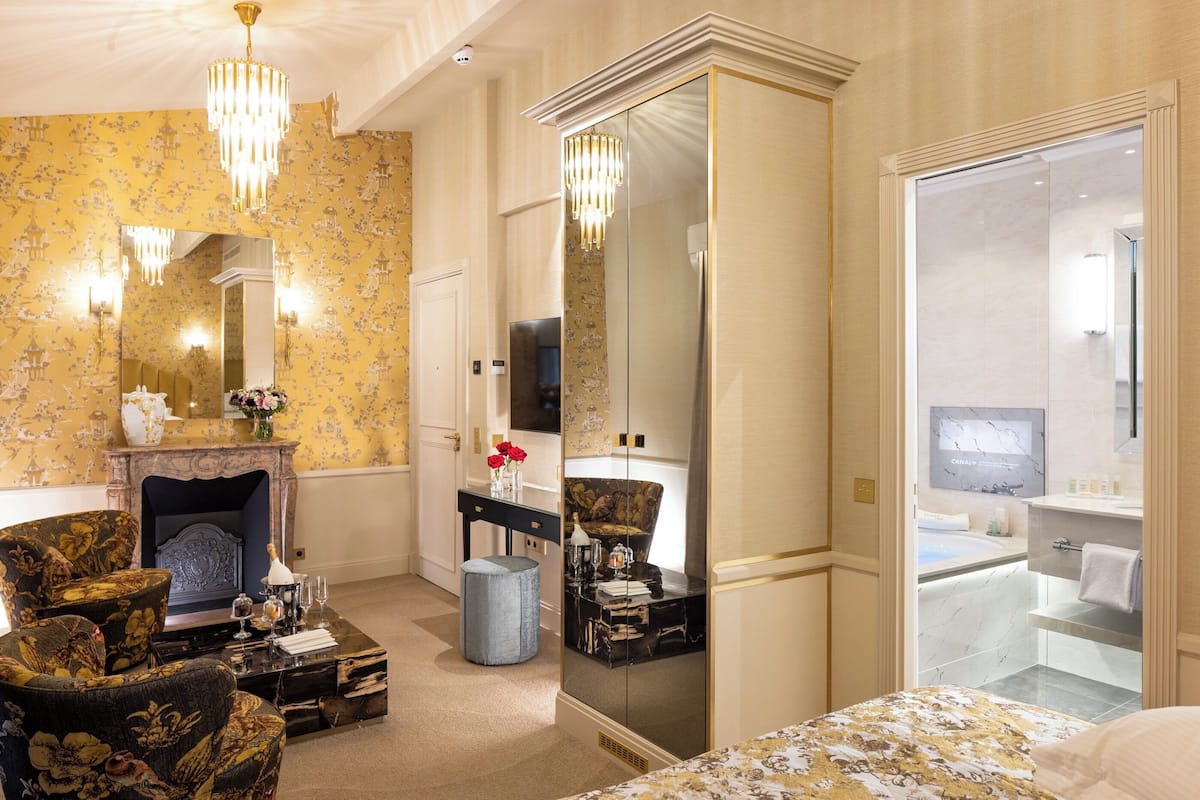 A hotel room with a large mirror, a fireplace, a bed, and a bathroom visible through an open door.