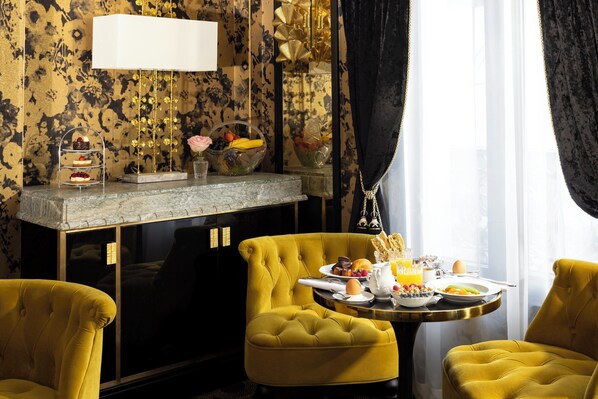 A dining area with a round table set for breakfast, yellow chairs, and a decorative wall with a floral pattern. - Manolita Paris (Paris)