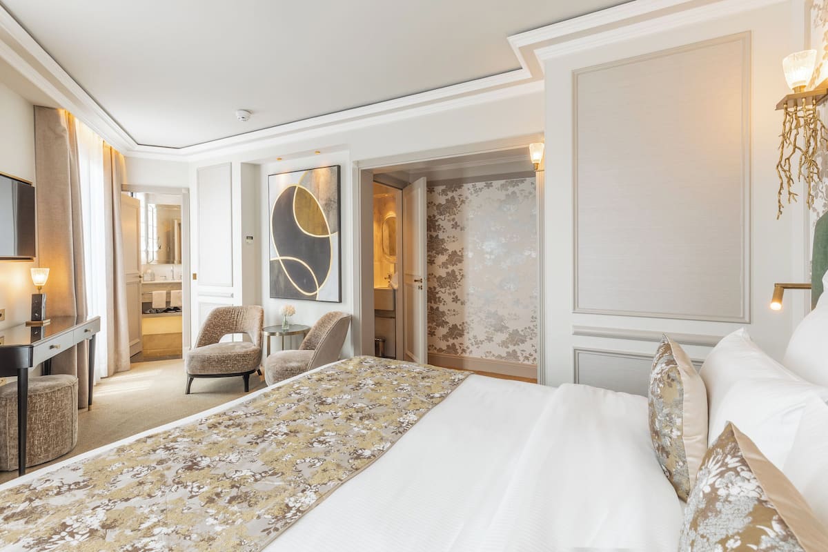 A hotel room with a large bed, a desk with a lamp, a chair, and a mirror.