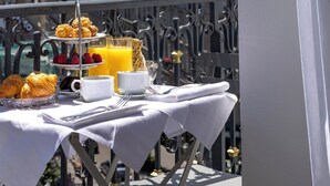 A balcony with breakfast setup, including croissants, fruit, and orange juice, overlooking a cityscape. - Manolita Paris (Paris)