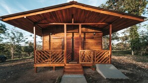 Una cabaña de madera con techo inclinado, un porche con barandillas de celosía y una pequeña entrada.