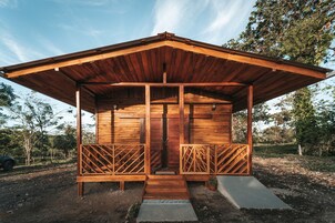 Una cabaña de madera con techo inclinado, un porche con barandillas de celosía y una pequeña entrada.