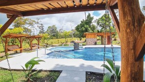 Una pérgola de madera con vistas a una piscina y una estructura de piedra al fondo.