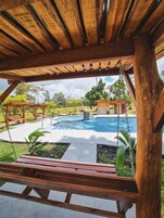 Una pérgola de madera con vistas a una piscina y una estructura de piedra al fondo.