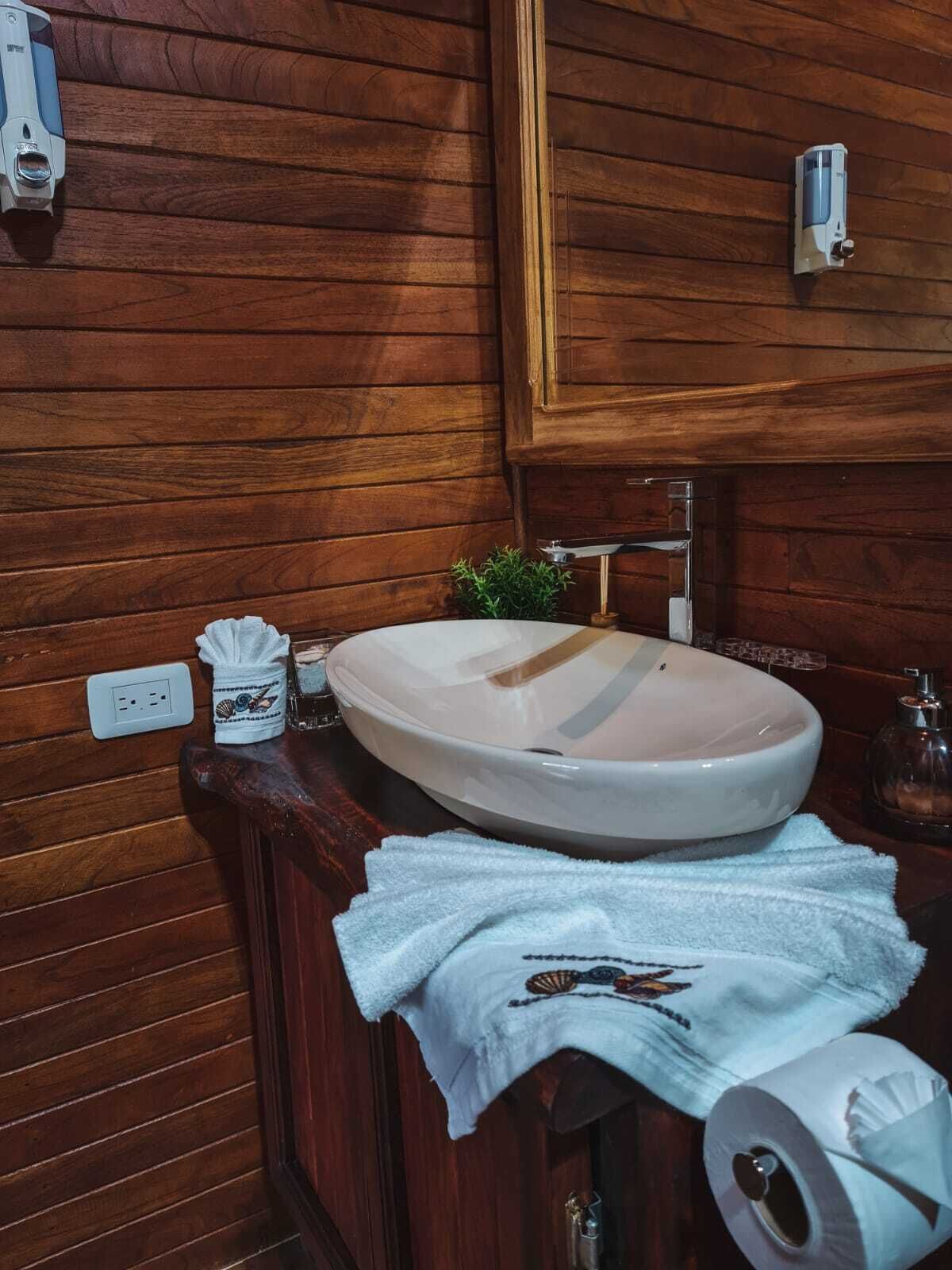 A wooden bathroom with a white sink, a towel, and a toilet paper roll.