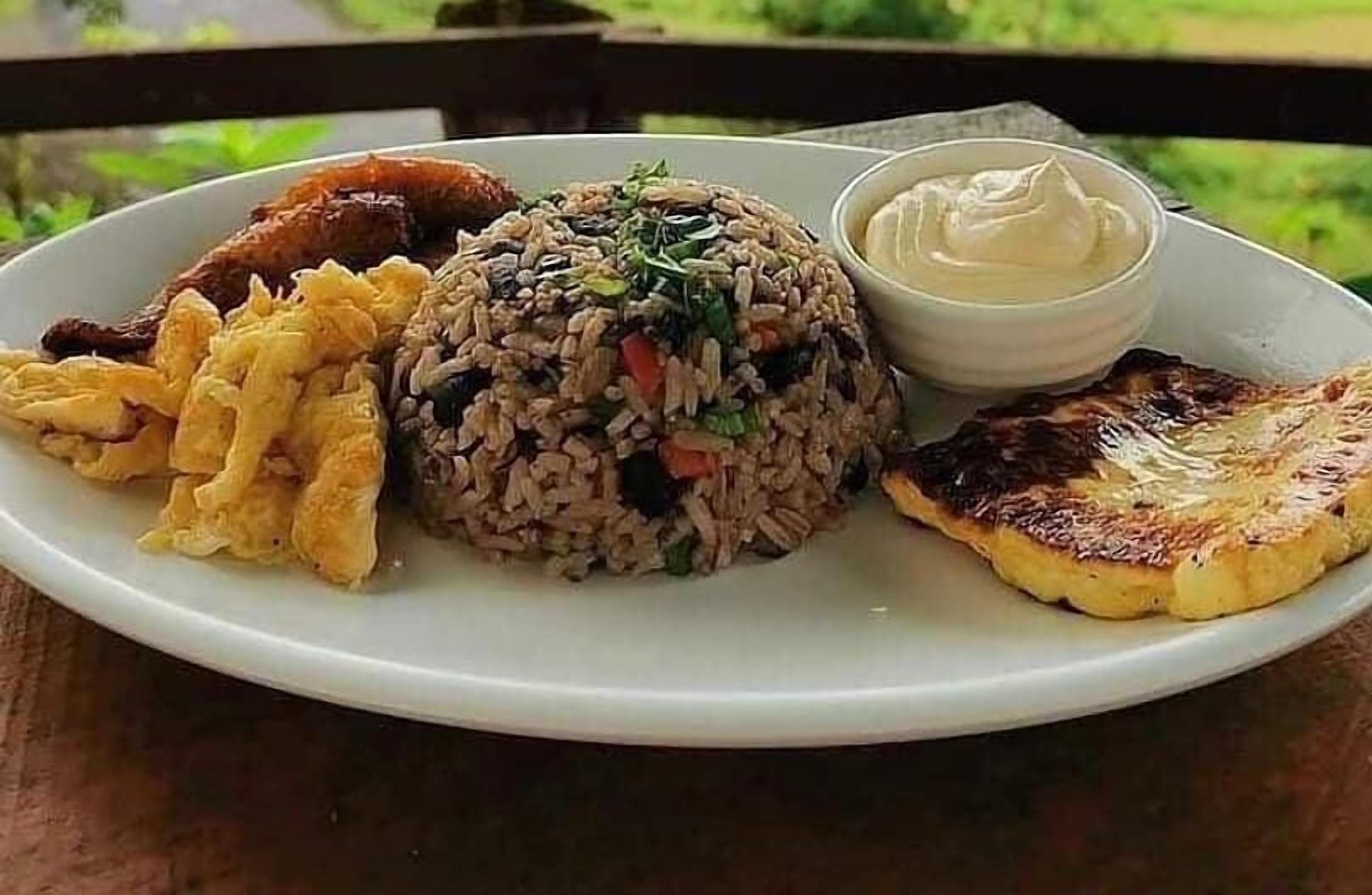 A plate of fried rice, fried plantains, and a side of sauce.