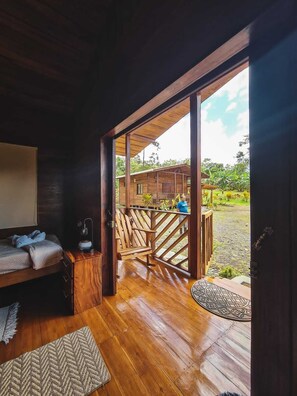 A wooden room with a bed, a desk, and a view of an outdoor deck and garden.