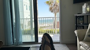 A room with a sliding glass door leading to a balcony with a view of the sea and a palm tree. - 3 Bedroom, Gulf View, Orange Beach Condo--A Boardwalk to Salt Life (Orange Beach)
