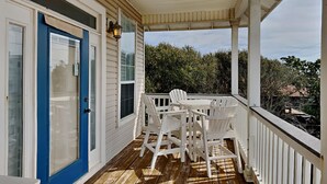 A covered porch with a table and chairs, a blue door, and a view of trees and buildings. - Camellia House by Southern Vacation Rentals (Santa Rosa Beach)