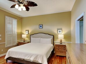 A bedroom with a large bed, two bedside tables with lamps, a ceiling fan, and two framed pictures on the wall. - Camellia House by Southern Vacation Rentals (Santa Rosa Beach)