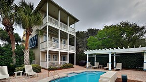 A two-story building with a pool, outdoor seating, and a pergola. - Camellia House by Southern Vacation Rentals (Santa Rosa Beach)