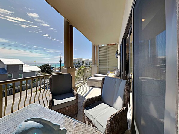A balcony with wicker furniture, a view of the ocean, and buildings in the background. - Abacos #304 by Southern Vacation Rentals (Santa Rosa Beach)