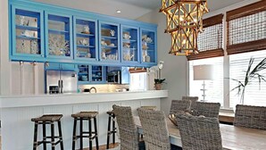 A kitchen with blue cabinets, a central island, bar stools, wicker chairs, and a hanging light fixture. - A Garden Cottage by Southern Vacation Rentals (Miramar Beach)