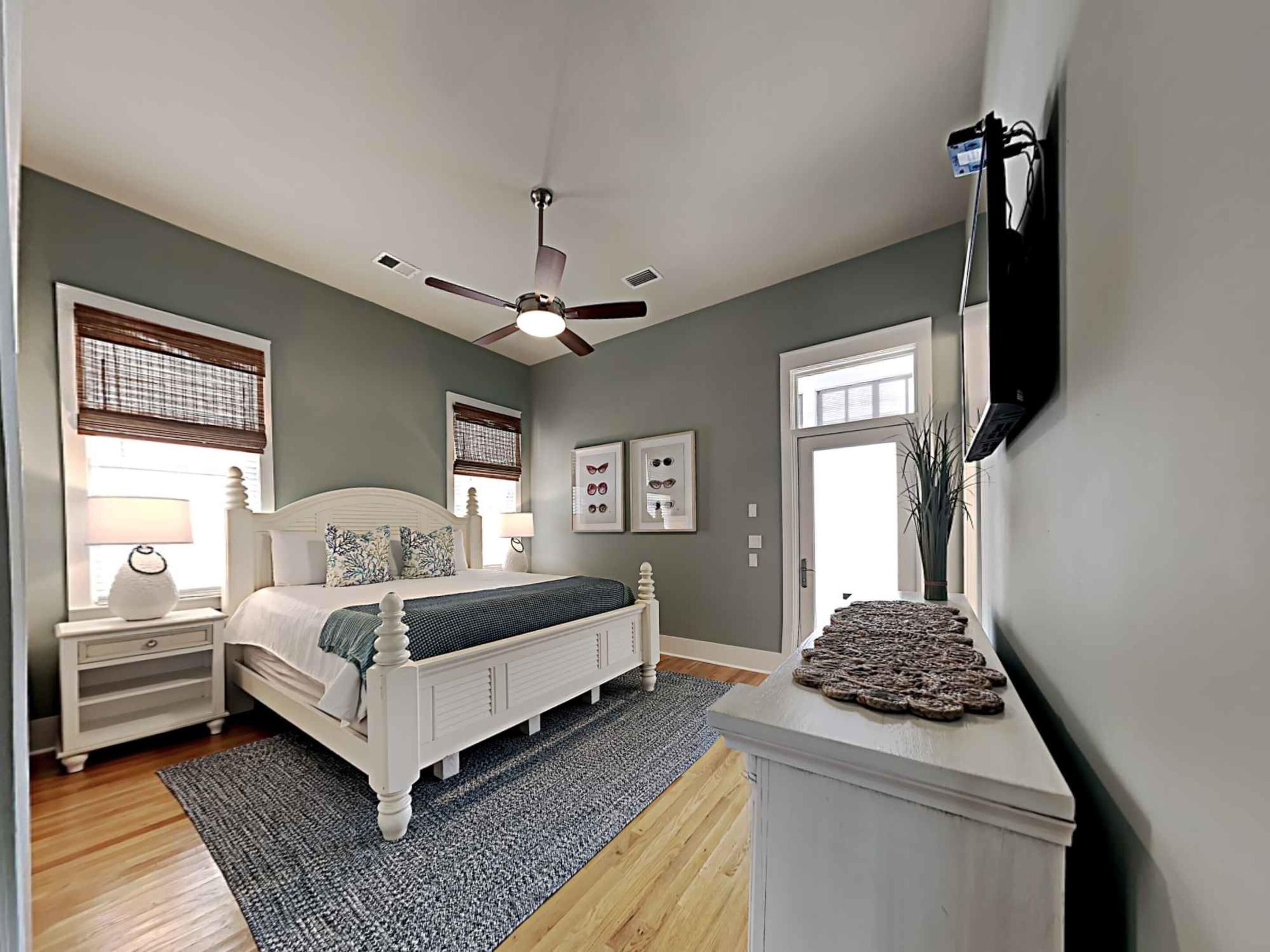 A bedroom with a bed, nightstands, a ceiling fan, and a TV mounted on the wall.