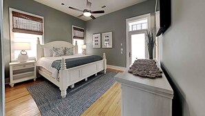 A bedroom with a bed, nightstands, a ceiling fan, and a TV mounted on the wall. - A Garden Cottage by Southern Vacation Rentals (Miramar Beach)