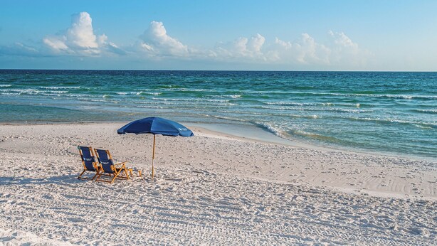 A beach with a clear sky, a blue umbrella, and a beach chair. - A Garden Cottage by Southern Vacation Rentals (Miramar Beach)