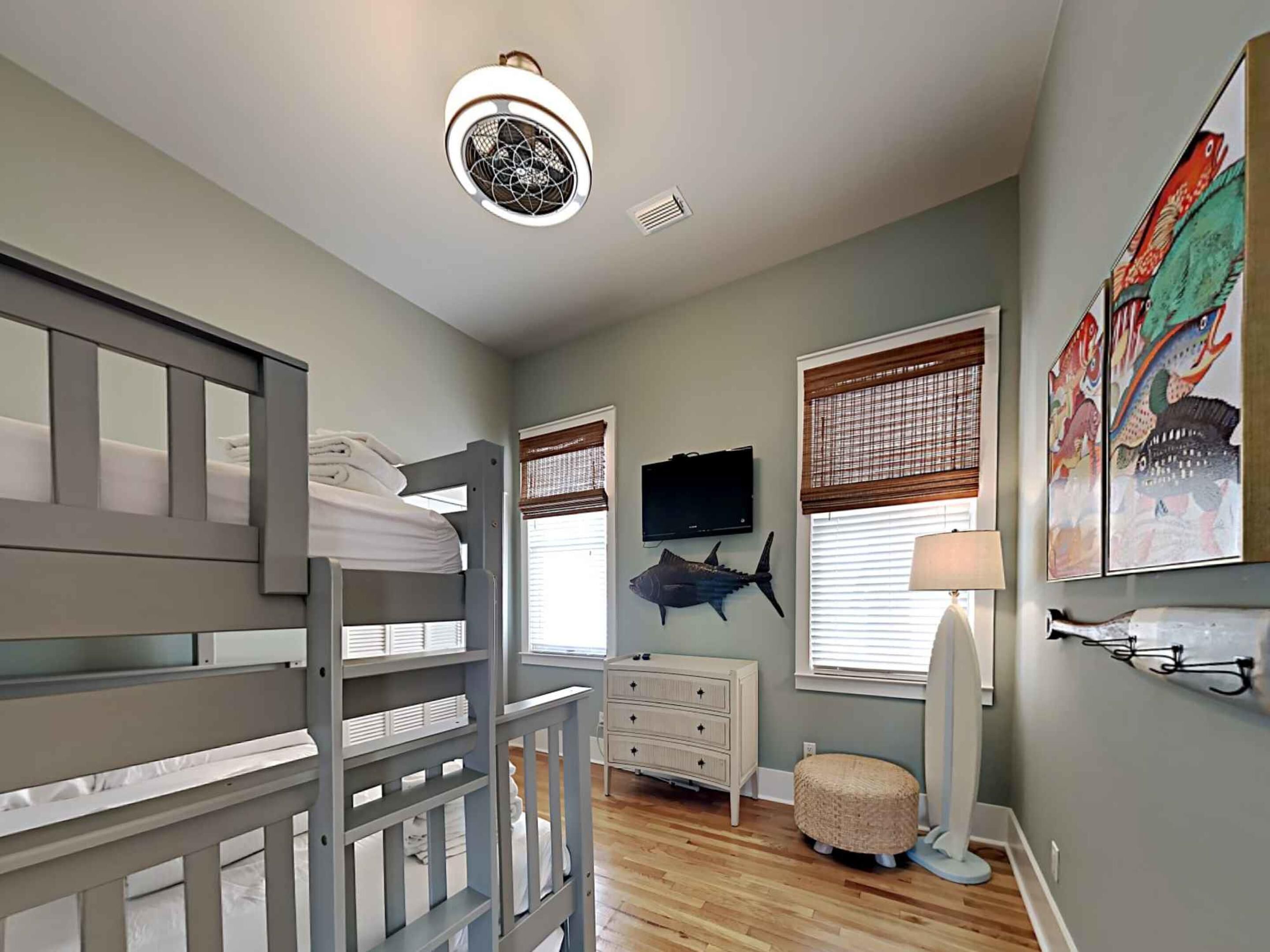 A child's bedroom with bunk beds, a dresser, a television, and wall art.