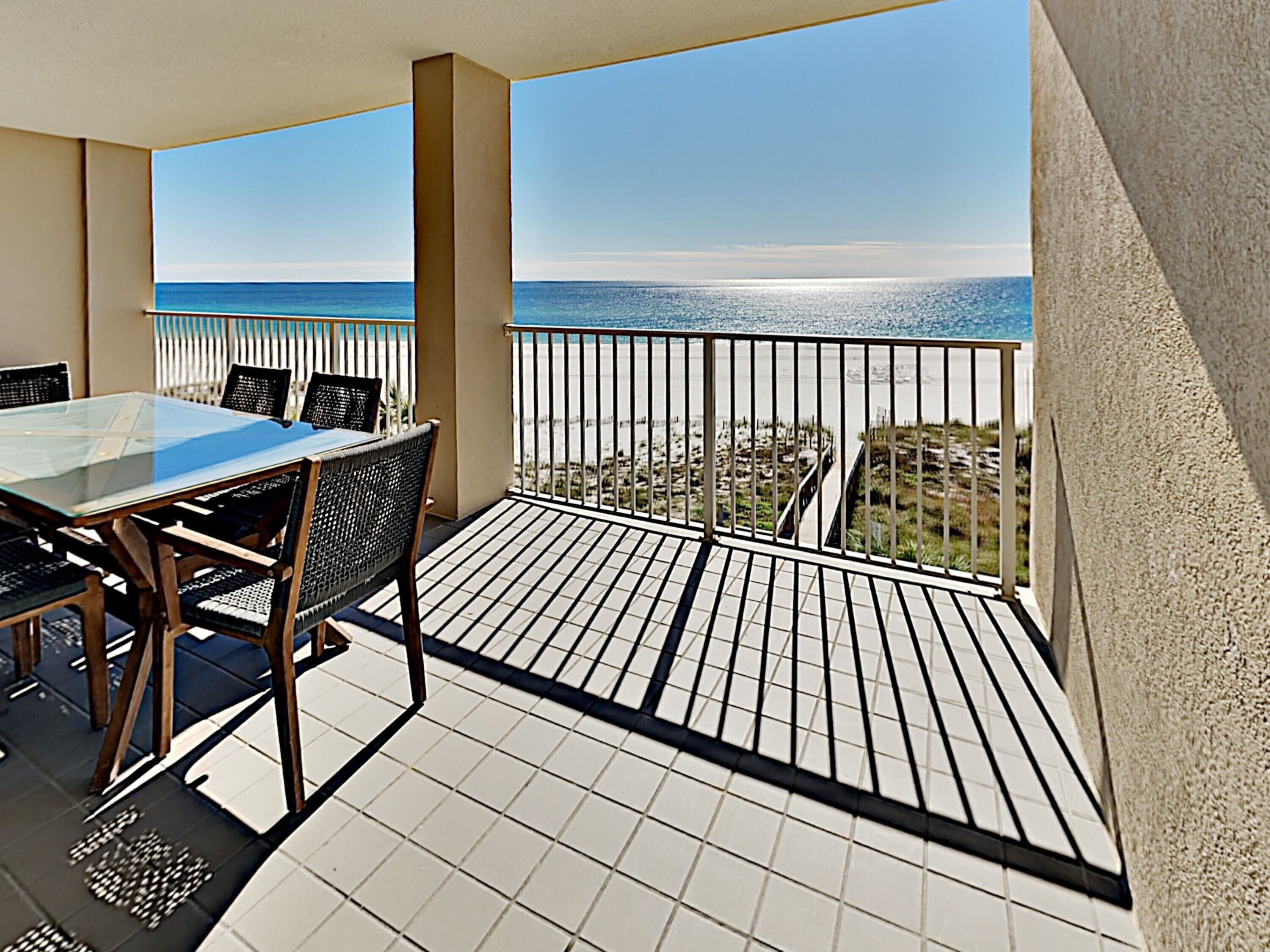 A balcony with a glass table and chairs, a tiled floor, and a view of the ocean.