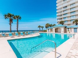 Piscina com espreguiçadeiras e palmeiras, cercada por um edifício com varandas.