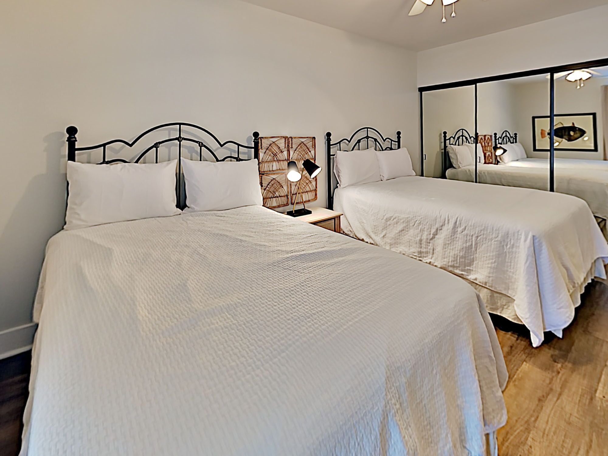 A hotel room with two beds, a nightstand with a lamp, and a large mirror reflecting the room.