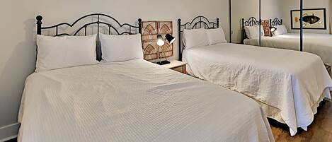 A hotel room with two beds, a nightstand with a lamp, and a large mirror reflecting the room.