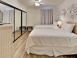 Habitación de hotel con cama, espejo, ventilador de techo y una pared con detalles decorativos.
