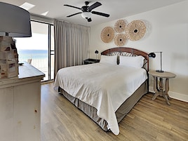 Un dormitorio con cama, ventilador de techo, mesita de noche, lámpara y vista al océano.