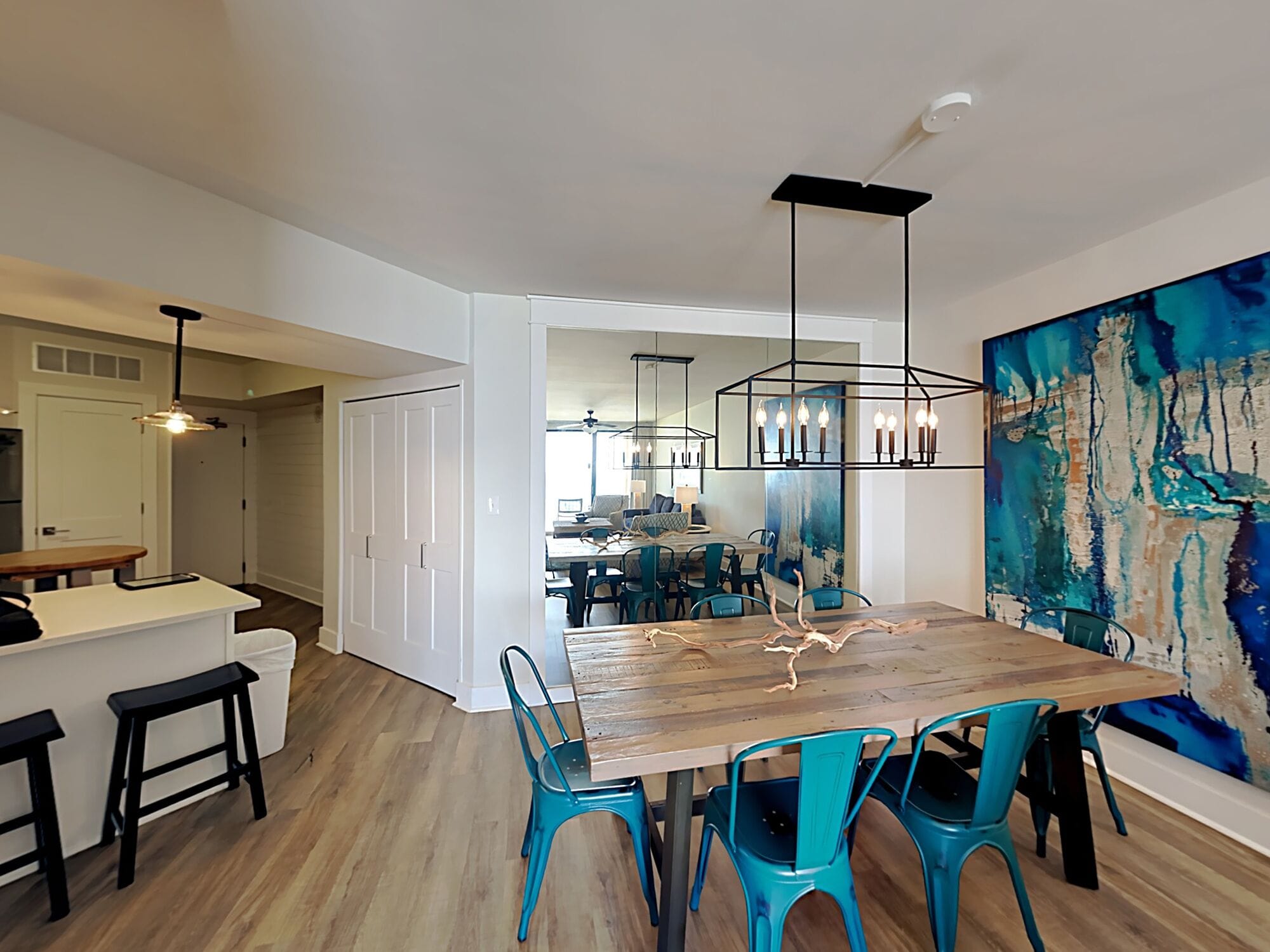 Un espace repas moderne avec une table en bois, des chaises de couleur turquoise et un luminaire suspendu noir.